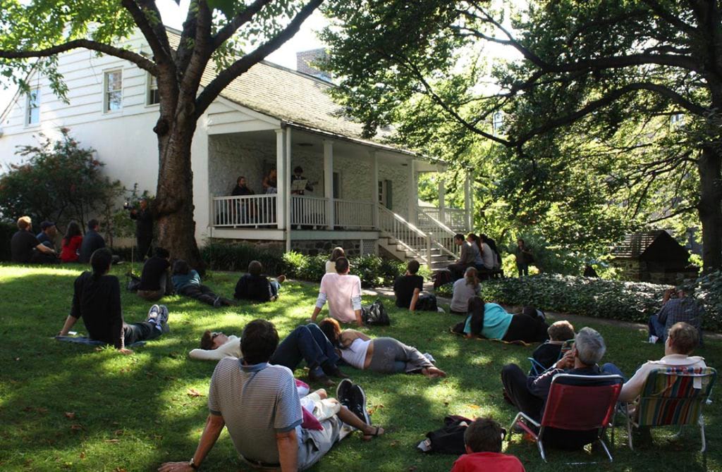 Visitors sitting on grass outside the Dyckman Farmhouse Museum