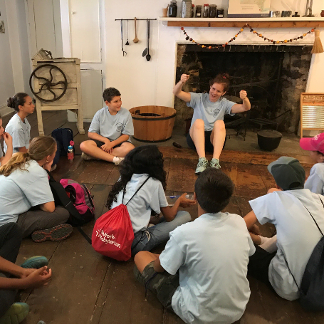 Students sitting on a floor in front of an old fireplace taking part in an educational program