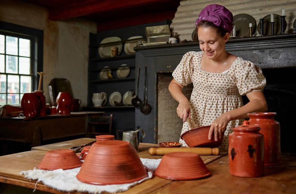 A woman in a historical outfit cooking inside the Historic Richmond Town