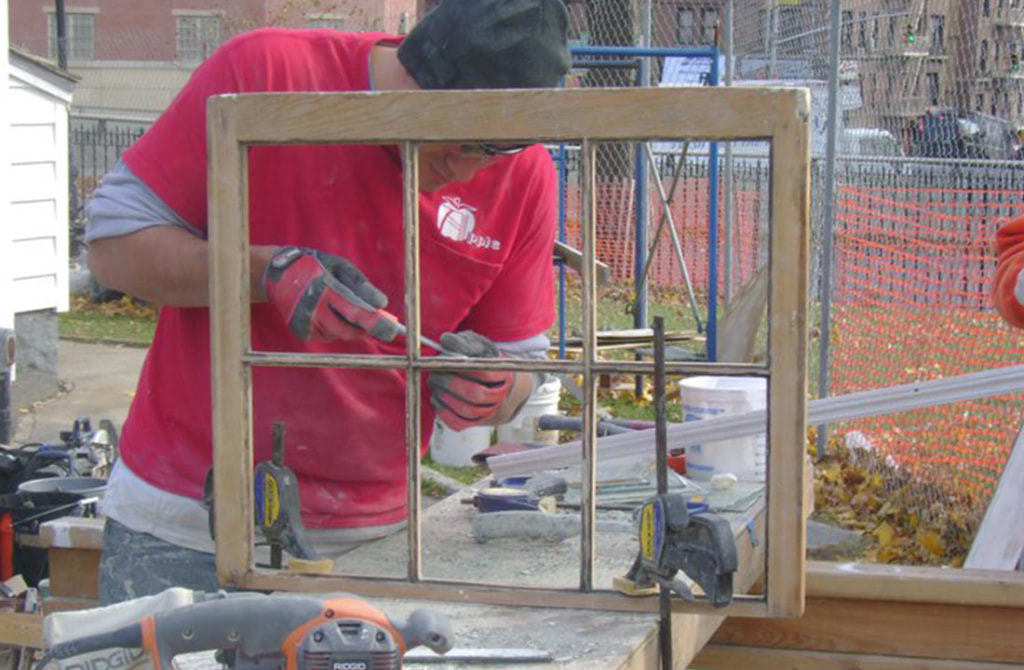 A man in red shirt working with a drill to fix a broken window