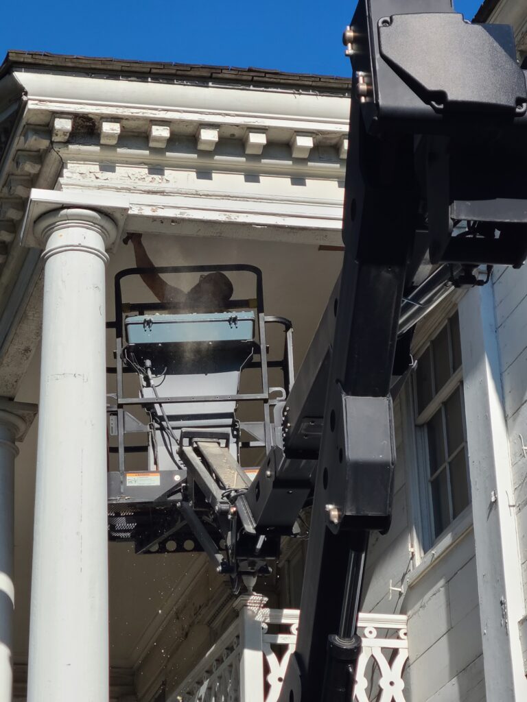 Man in a mechanical lift underneath a white historic house portico.