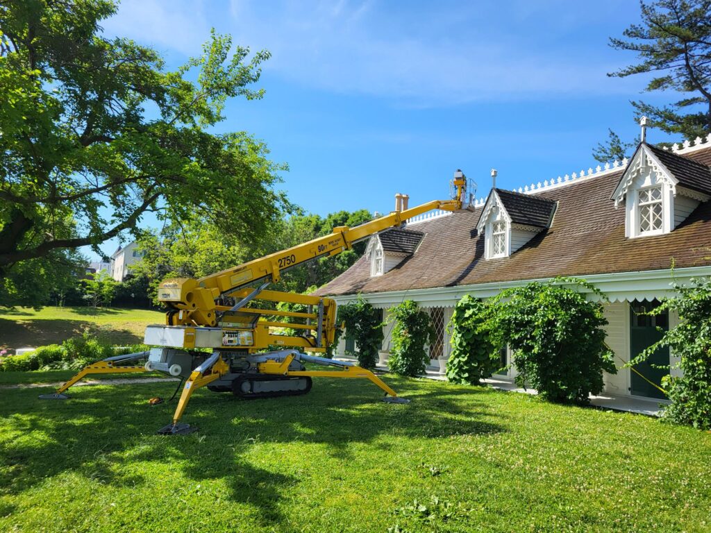 White house with brown roof in green lawn with yellow lift in front. 