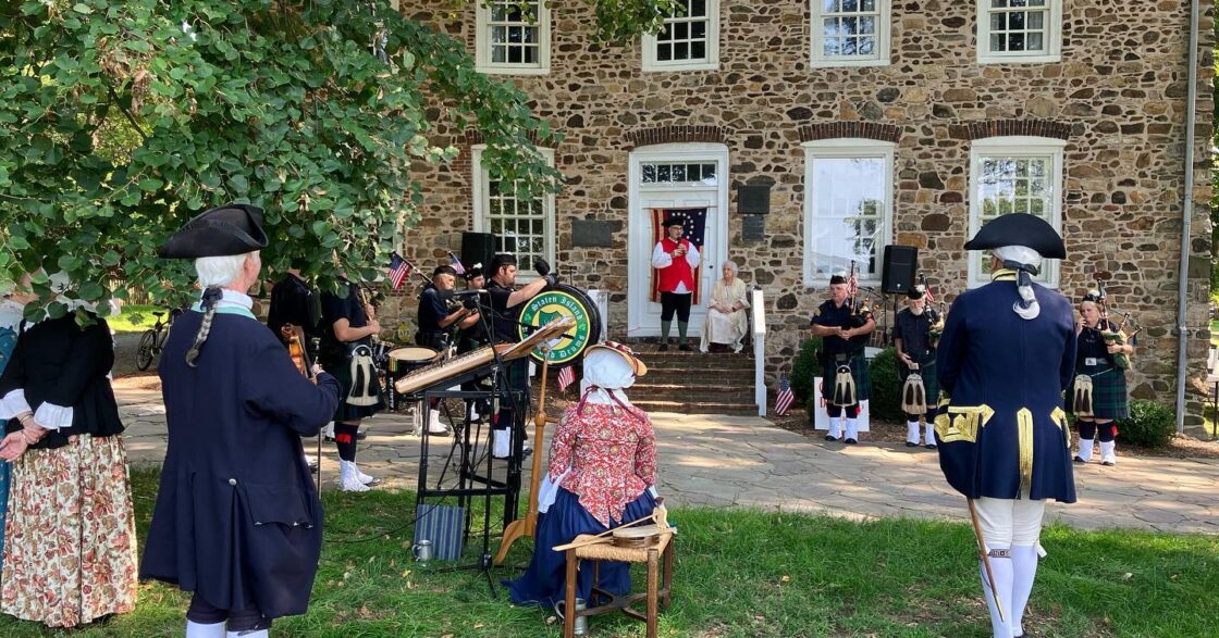 Stone historic house in background with modern individuals in historic dress playing instruments.