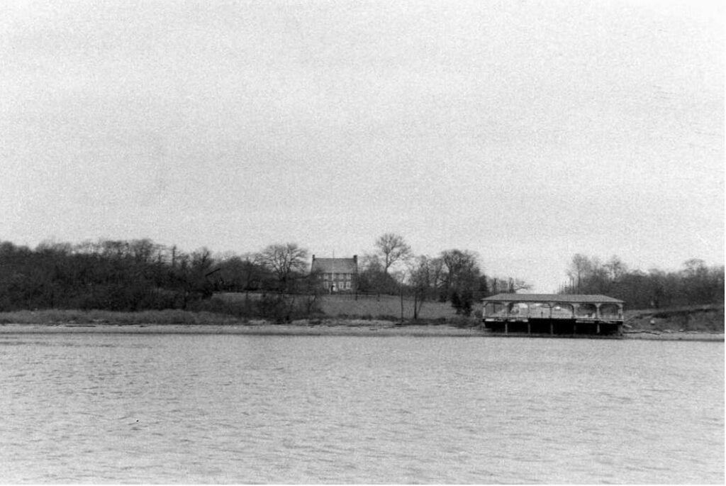 Black and white photo of a historic house on a hill viewed from the water. 