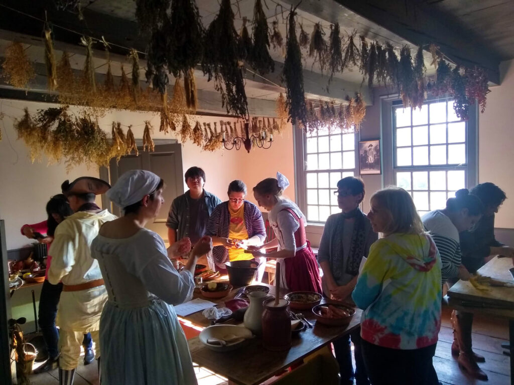 School group surrounding a table inside the historic farmhouse with dry herbs hanging from the ceiling. 