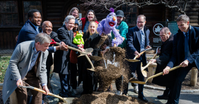 Group of people and two puppets lifting and throwing shovels of dirt