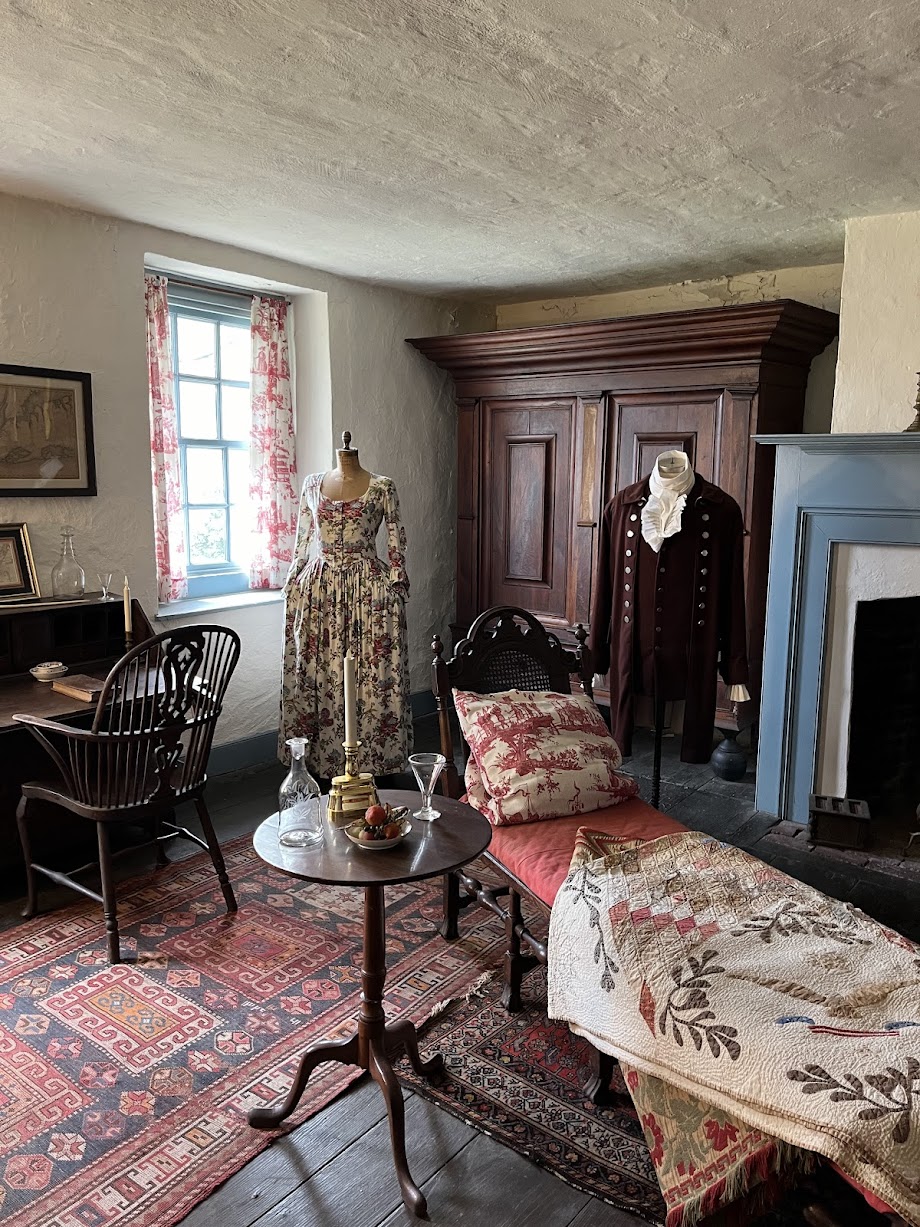 White room with two mannequins in period dress surrounded by colonial funiture.