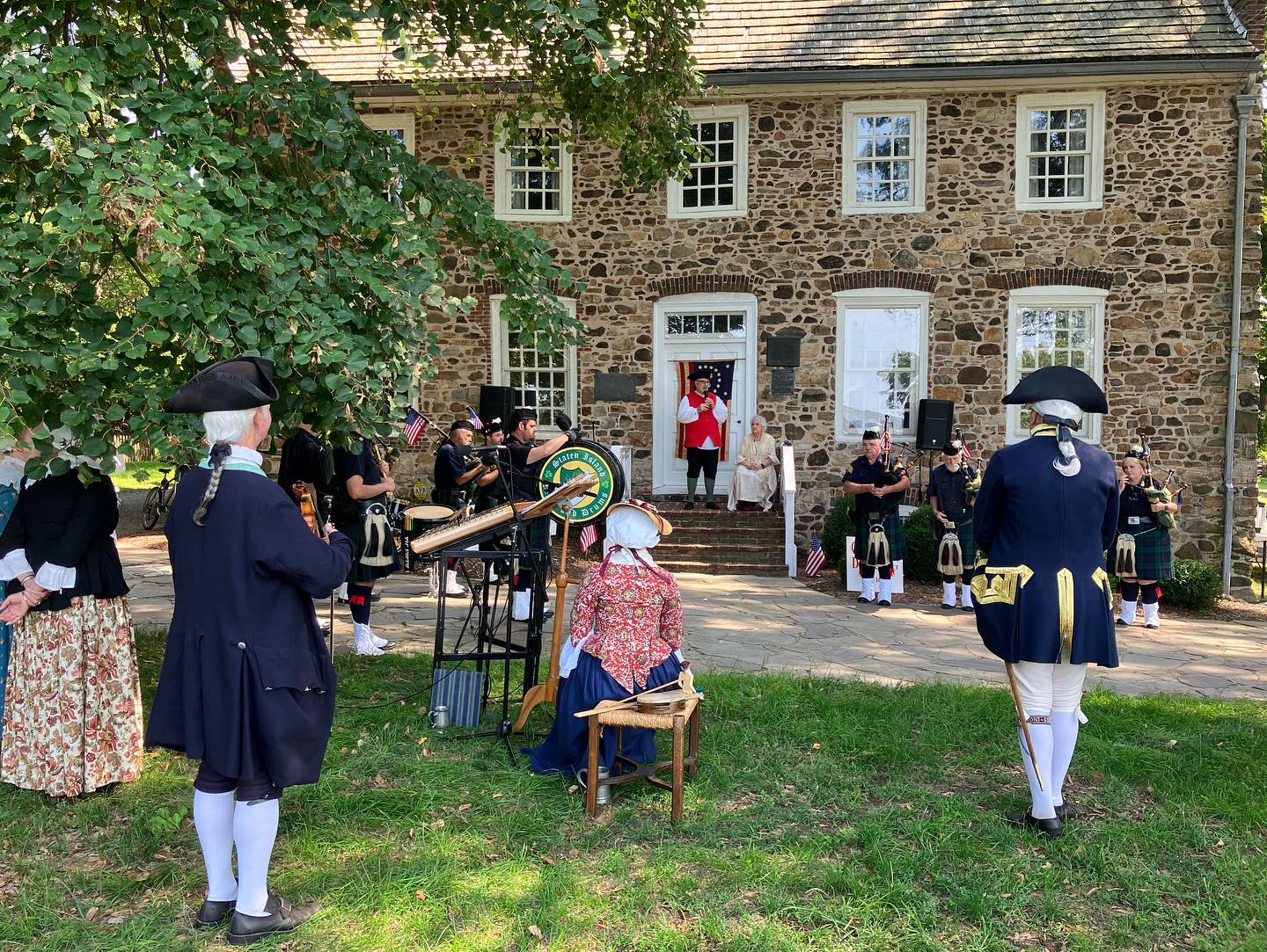 Group of people in colonial dress in front of a stone building.